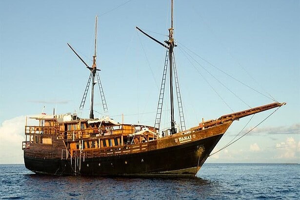 Damai I liveaboard, a traditional Indonesian sailing yacht, at anchor on calm water