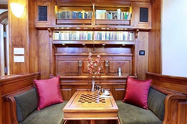 Indoor salon on the Adelaar liveaboard with a chess table and teak wood paneled bookshelves