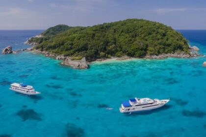 aerial view of two liveaboard boats anchored in turquoise water beside a forested island in Thailand