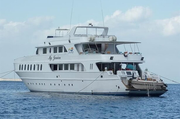 Side profile of the My Jessica liveaboard, multi-deck vessel moored with tender boat astern