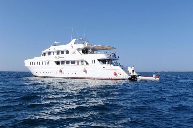 My Jessica liveaboard anchored offshore with a tender boat pulled alongside the stern