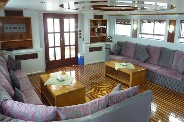 Saloon lounge on the MY Jessica liveaboard with grey sofas, inlaid wood floor and doors to the deck