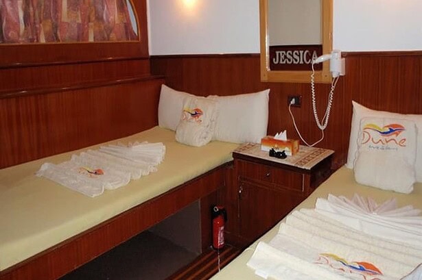 Twin cabin on the MY Jessica liveaboard with two beds dressed in logo pillows and folded towels