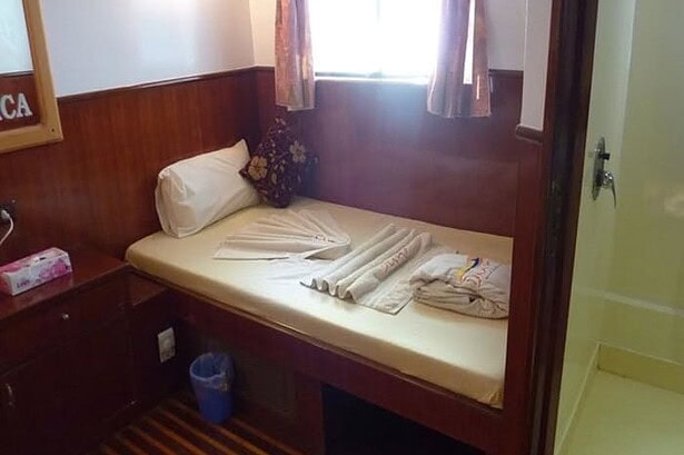 Single bed cabin on the MY Jessica liveaboard with folded towels and a bedside cabinet