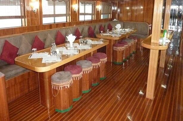 Wood paneled dining saloon on the MY Jessica liveaboard with red velvet stools and table settings