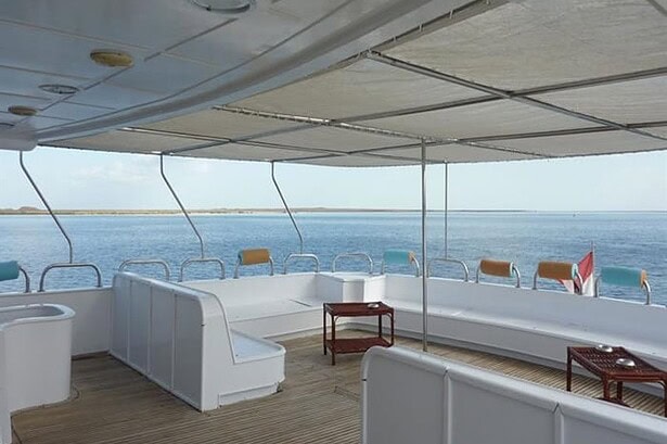 Shaded aft deck aboard the My Jessica liveaboard with curved lounge seating and a chiller box along the rail