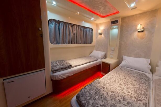 Twin bed cabin aboard a Red Sea liveaboard with red accent lighting and striped curtains over the window