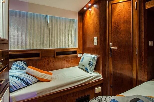 Single bed in a wood paneled cabin on the Blue Planet 1 with a cabin door alongside