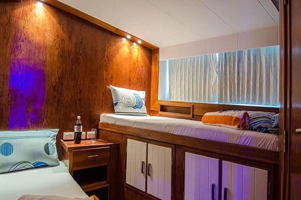 Twin cabin on the Blue Planet 1 with wood paneling and colorful bedding under warm lighting