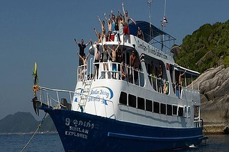 the liveaboard Similan Explorer packed with divers waving from the top deck, anchored by a rocky island