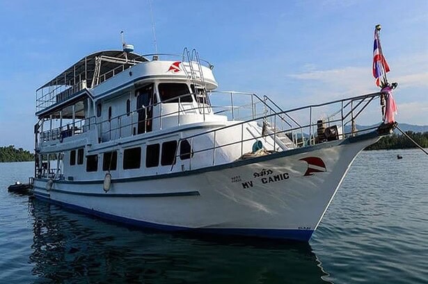 The MV Camic liveaboard at anchor, showing its white multi-deck hull and Thai flag at the stern