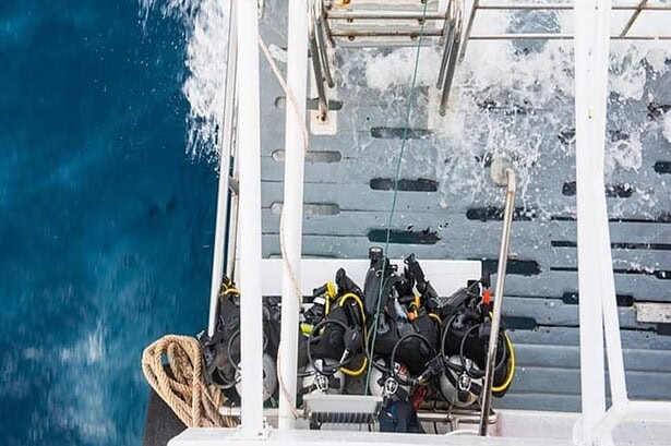 Overhead view of the MV Camic's dive deck loaded with scuba gear as the boat cuts through blue water
