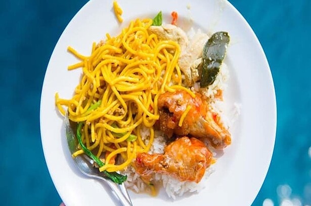 Plate of noodles, curry chicken and rice served aboard the MV Camic liveaboard, held above blue water