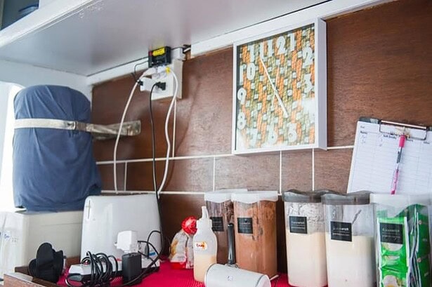 Coffee and tea station on the MV Camic with drink dispensers, a wall clock and a sign-up sheet