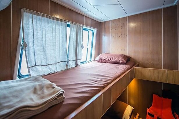 Wood paneled single berth cabin on the MV Camic with a life vest tucked underneath the bed