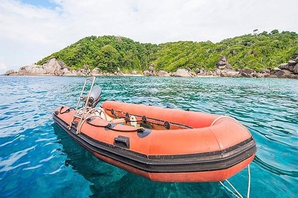 An orange dive tender anchored in turquoise water off a granite outcrop in the Similan Islands