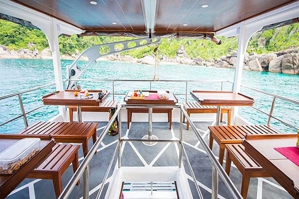 Open air dining deck aboard the MV Camic with wooden tables overlooking turquoise water and green islands