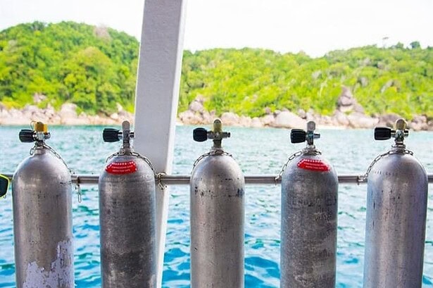 Row of scuba tanks racked on the MV Camic's dive deck with the Similan Islands coastline behind