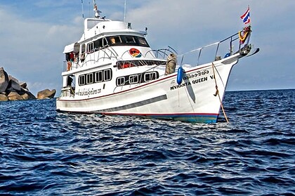the liveaboard Manta Queen 6 anchored near rocky outcrops, a Thai flag flying from the bow