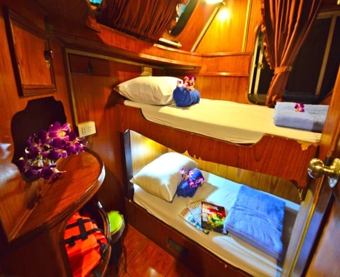 wood paneled bunk cabin aboard Manta Queen 6 decorated with fresh orchids and a life jacket by the beds