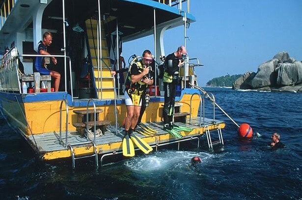 Divers giant-striding off the MV Marco Polo's dive deck into the sea near a granite island