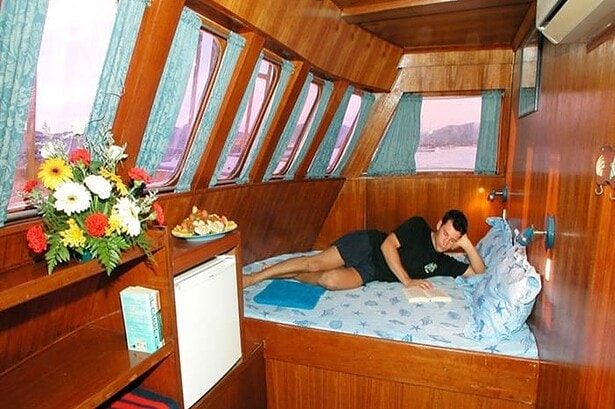 Guest reading in a wood paneled cabin aboard the MV Marco Polo with flowers and a mini fridge