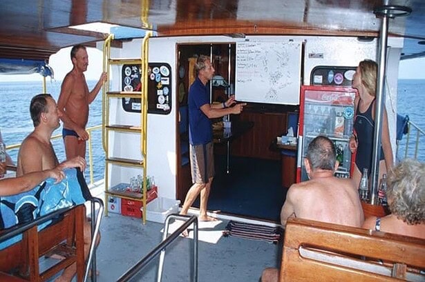 Dive guide briefing guests using a whiteboard chart aboard the MV Marco Polo