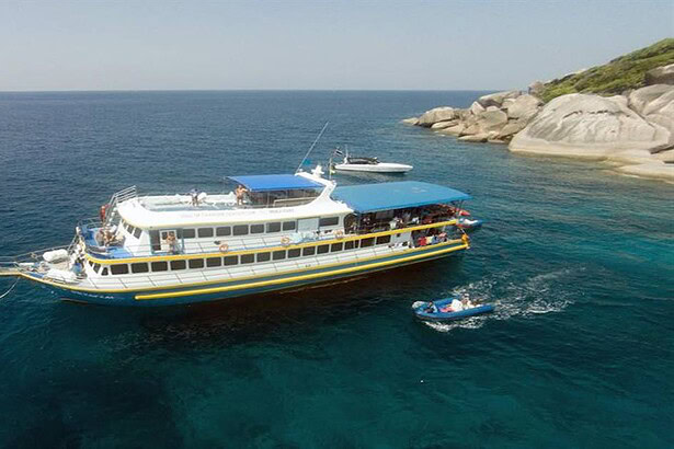 The Oktavia liveaboard anchored beside a rocky island with a dive tender alongside