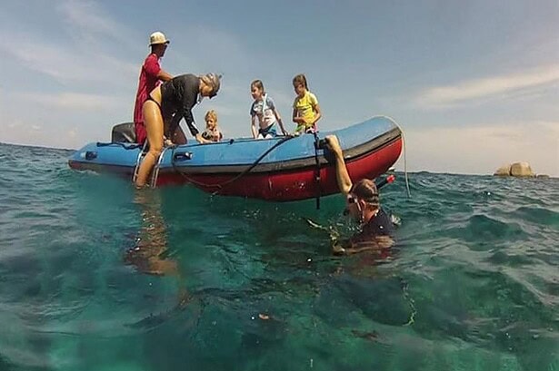 Crew helping a snorkeler back into the Oktavia's dinghy while children look on from the boat
