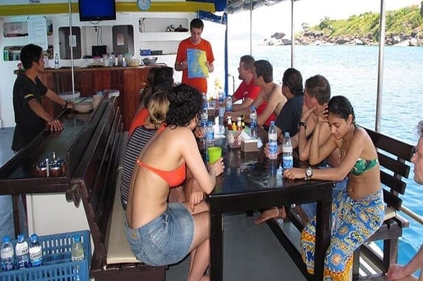 Dive guide briefing guests on the day's dive site using a laminated map at the boat's bar
