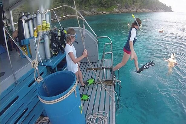 A guest leaping off the Oktavia's dive deck into clear water beside a rack of scuba tanks