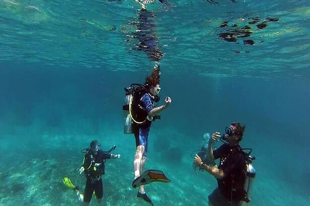 A diver blowing bubble rings during a safety stop while two buddies watch nearby