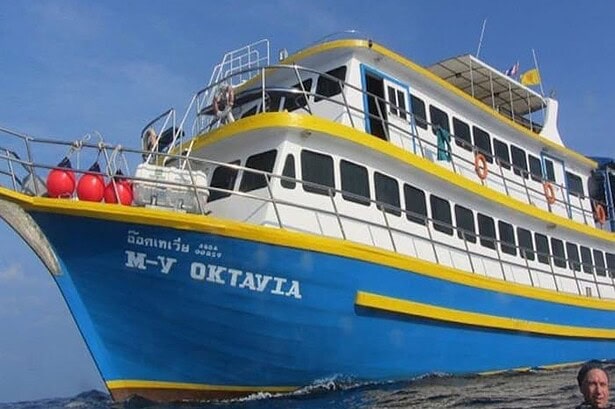 Side view of the Oktavia liveaboard anchored at sea with a diver surfacing in the foreground
