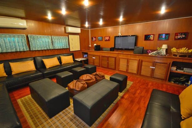 Wood paneled saloon lounge with black leather sofas and a TV on the Manta Queen 3 liveaboard