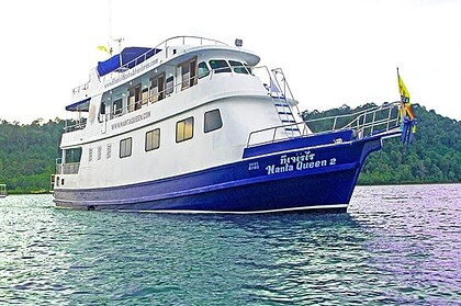 Manta Queen 2 liveaboard boat reflected in calm water near a forested shoreline