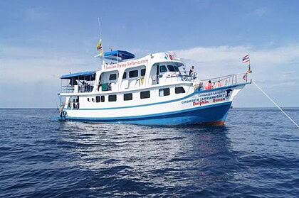 The Dolphin Queen liveaboard anchored in calm water, flying the Thai flag
