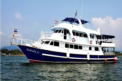 The Andaman Tritan liveaboard moored near a rocky Thai coastline under blue sky