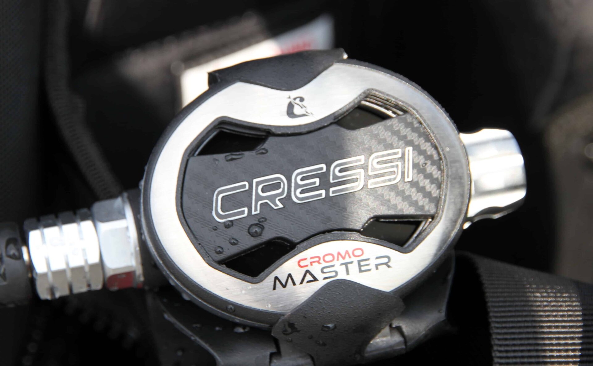 Cressi AC25 Master Cromo second stage resting on a black BCD, water beading on its carbon-look cover