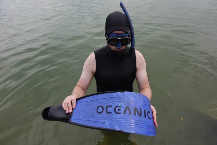 Testing The Oceanic Predator In The Lake Our reviewer in a wetsuit, hood and mask holding the Oceanic Predator fin blade above the water