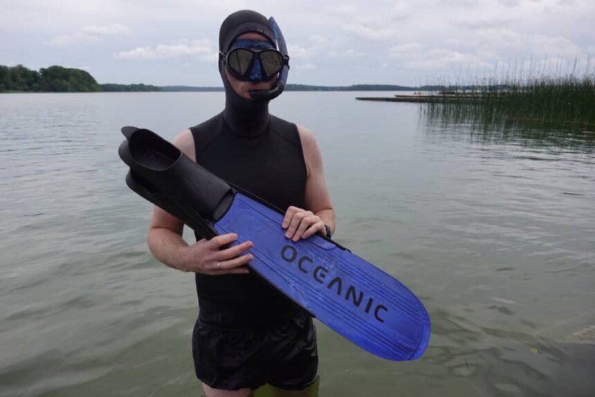 Oceanic Predator Fins Ready For Testing DIVEIN tester in a wetsuit and mask standing in a lake holding a pair of Oceanic Predator fins