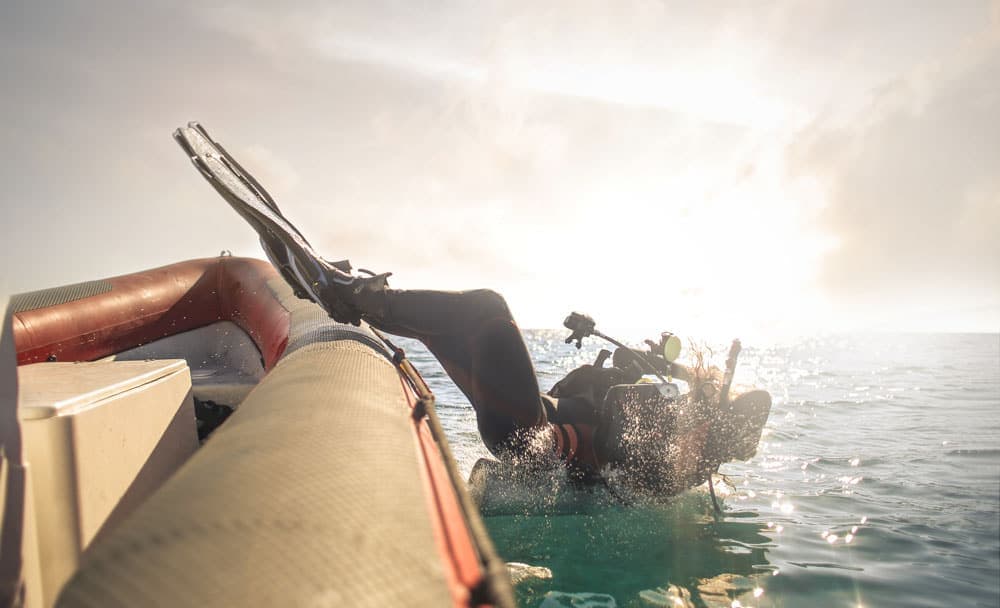 Diver backrolling off an inflatable boat into open water at sunrise