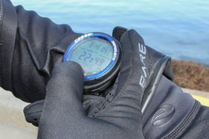 Our tester checking a round Cressi wrist dive computer display through thick gloves at the water's edge