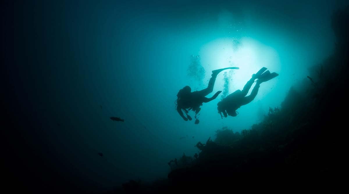 Instructor and student silhouetted underwater with bubbles during open water training