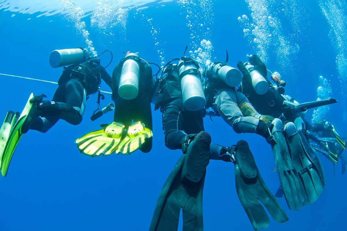Group of divers holding a descent line together, fins and tanks visible underwater