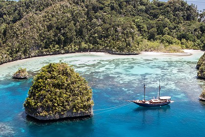 Aerial view of a liveaboard dive boat anchored among limestone islands in a turquoise lagoon