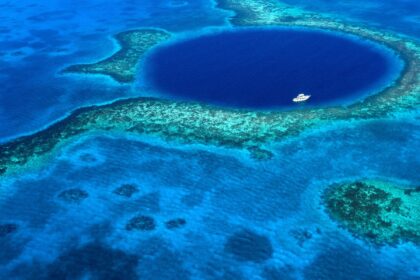 Aerial view of the Great Blue Hole in Belize, a dark circle in the reef with one boat on it