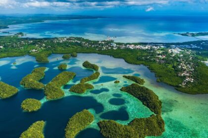 Aerial view of forested islets, turquoise lagoons and a coastal town in Micronesia