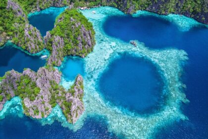 Aerial view of limestone karst cliffs, deep blue lagoons and outrigger boats in the Philippines