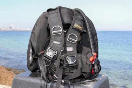 Zeagle Ranger BCD standing upright on a concrete block by the sea, harness, D-rings and inflator hose visible