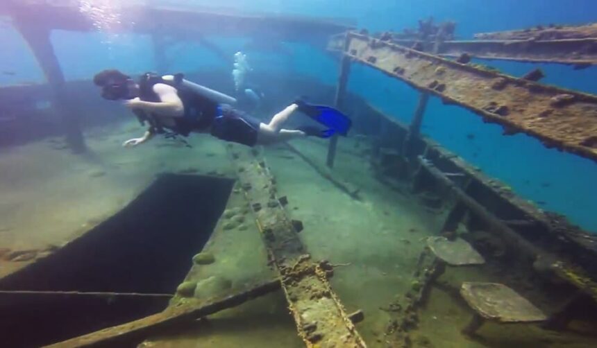Scuba diver finning over the sunken beams and wreckage at The Boot dive site in Barbados